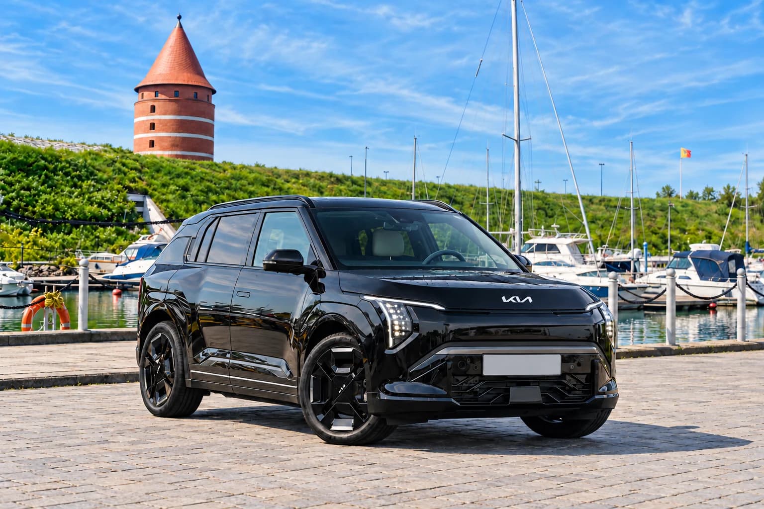 Black Kia EV3 by a harbour quay, with boats and a red-brick tower in the background